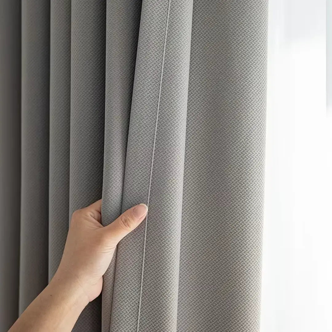 Mão segurando as pregas da Cortina Valeriana cinza junto à luz branca da janela