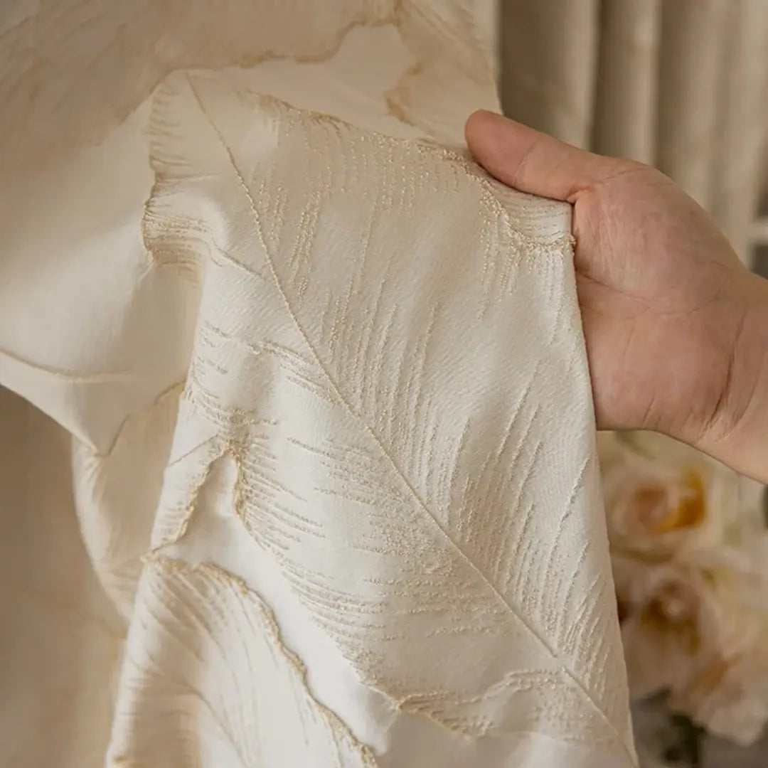 Cortina Golden Leaf bege com mão segurando o tecido bege para evidenciar o jacquard de folhas em relevo