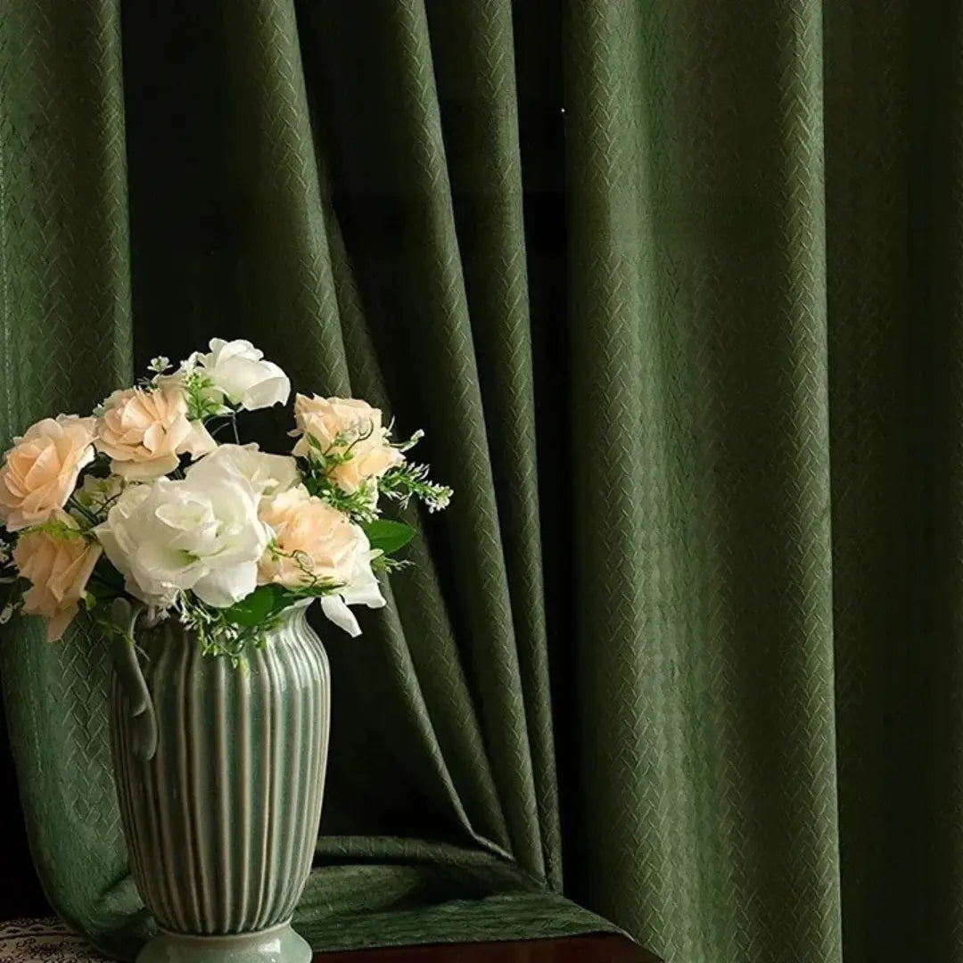 Cortina Lysander verde fechada atrás de vaso com flores claras, com pregas profundas em verde escuro