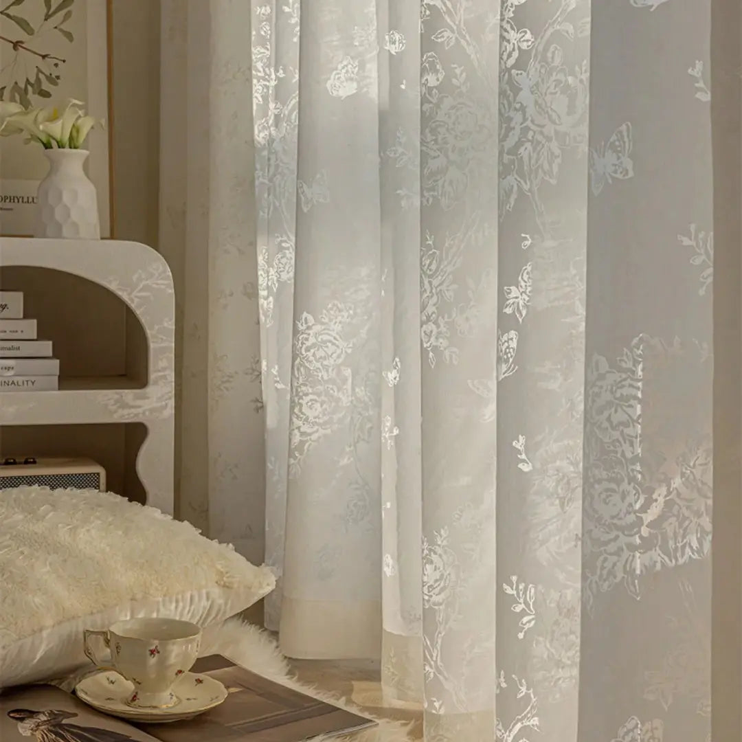 Painel Delicate Bloom bege ao lado da cama, com desenhos florais visíveis contra a luz