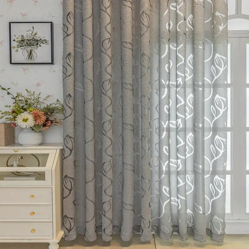 Cortina Folhas de Outono prateada vista lateral ao lado de cômoda, com folhas vazadas e pregas cinza bem definidas