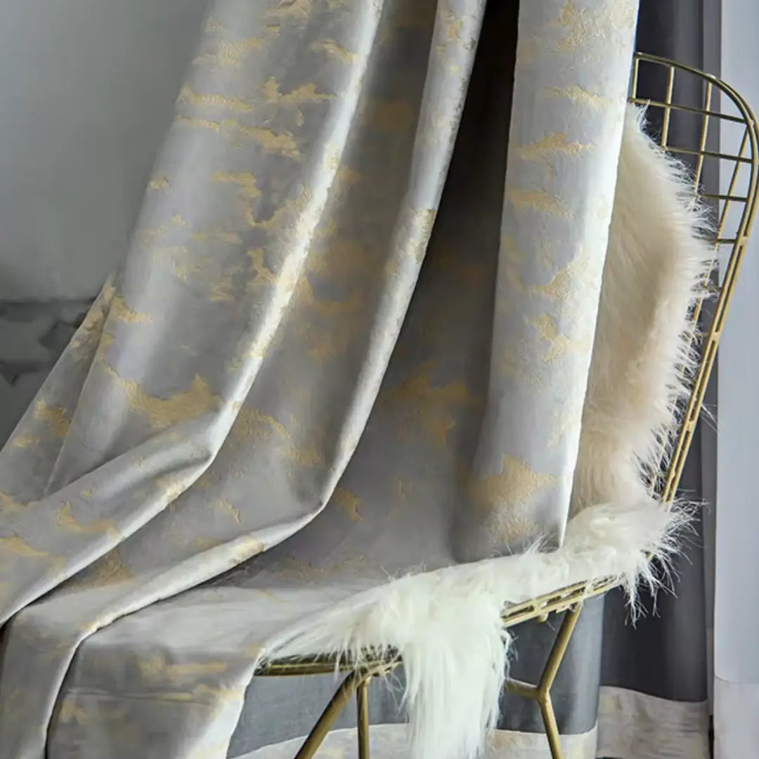 Cortina Noctua bege e dourada drapeada sobre cadeira com manta felpuda, exibindo brilho e estampa dourada