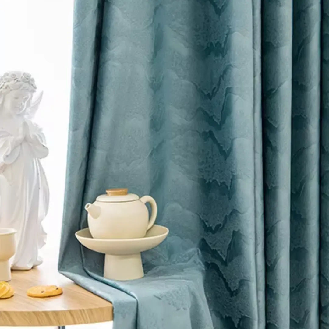 Cortina Verdôme azul com relevo tonal, ao lado de mesa decorada com bule e xícara
