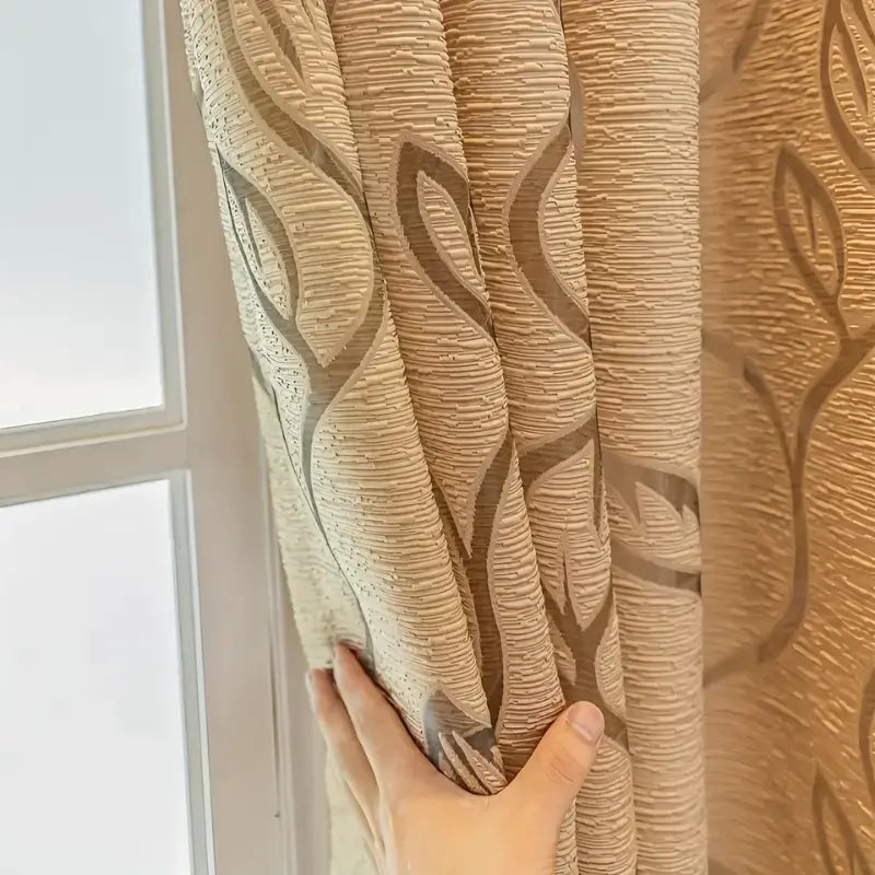 Cortina Folhas de Outono dourada com mão reunindo as pregas e mostrando o relevo ondulado do tecido dourado