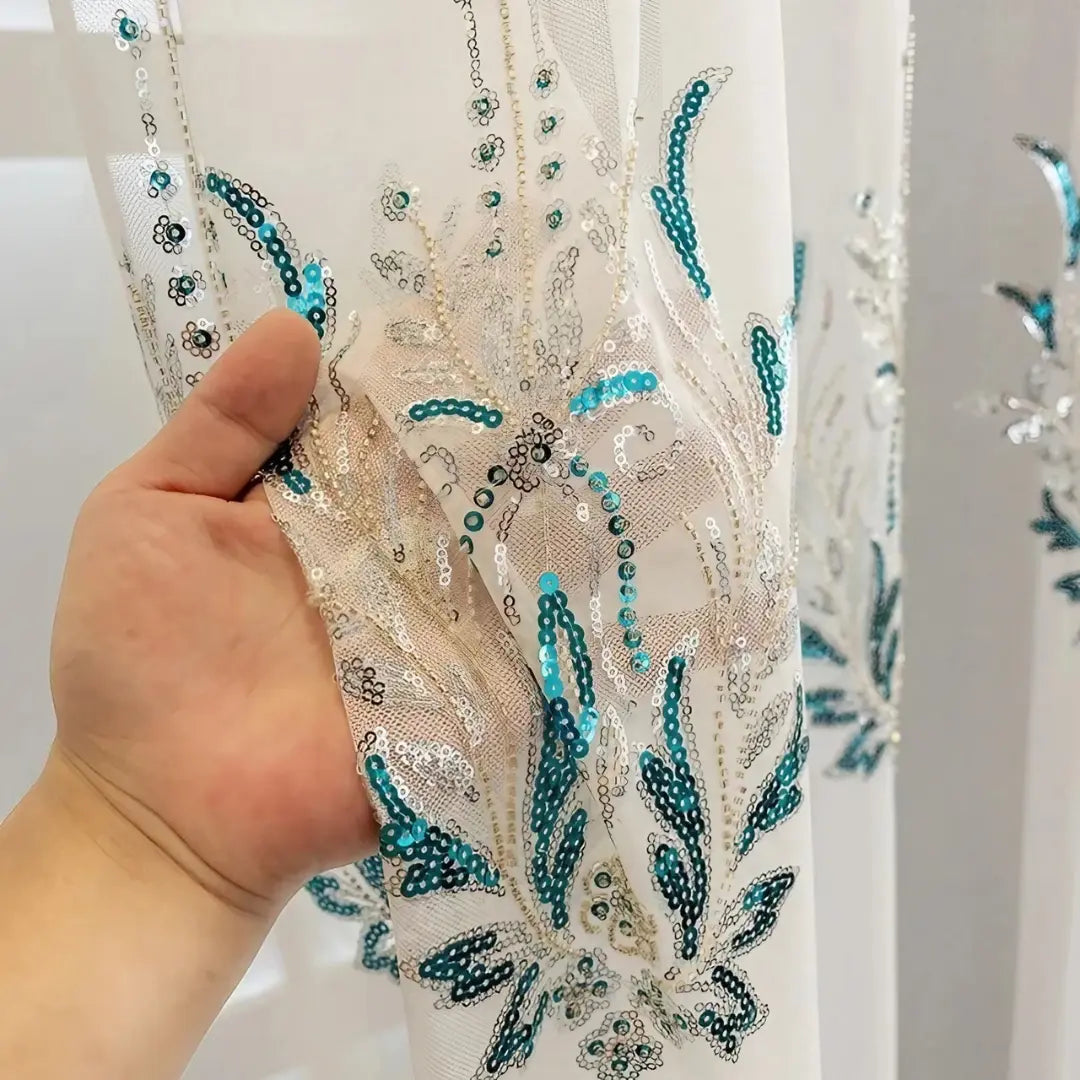 Bordado da Éléonore em close, com folhas azul-turquesa, fios prateados e pequenos pontos brilhantes