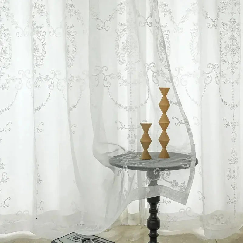 Cortina Alurea branca atrás de mesa lateral, com transparência suave e arabescos bordados