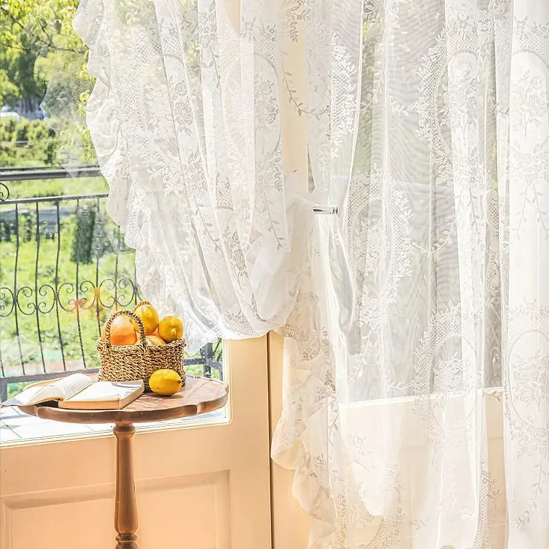 Cortina Valerys de renda branca junto à varanda, com mesa redonda e frutas à frente
